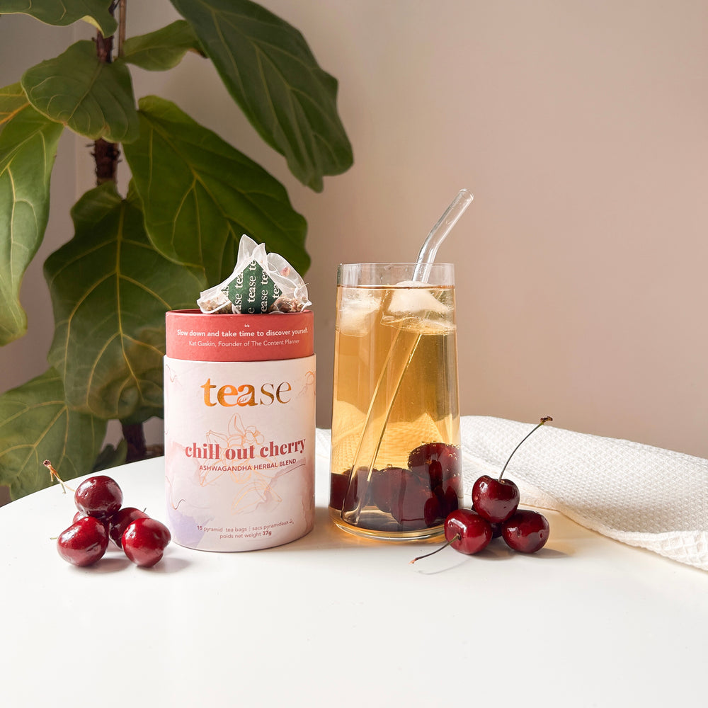 Tease Wellness Chill Out Cherry tea blend in a pink tube with cherries, served in a glass with ice and straw.