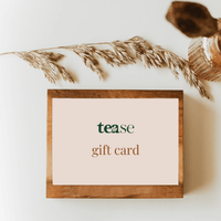 Tease Wellness gift card on wooden stand with beige background and dried pampas grass decor.